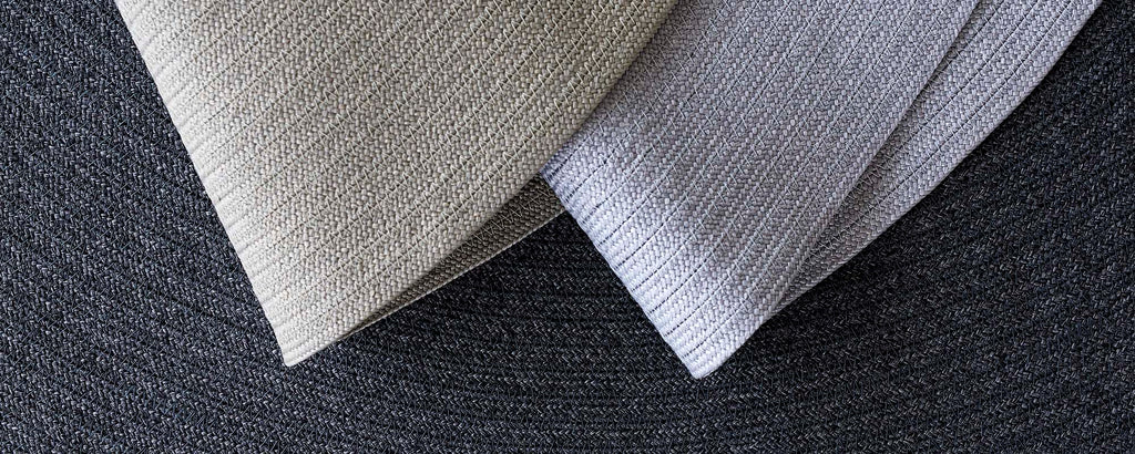 Two textured fabric pieces in neutral tones, placed diagonally on a circular dark background, showcasing their subtle patterns.