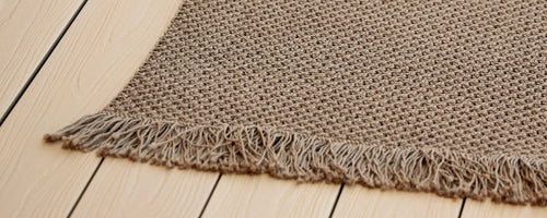 Close-up of a textured knit fabric with fringe edges, showcasing a warm, neutral color. Ideal for adding comfort and style to any space.
