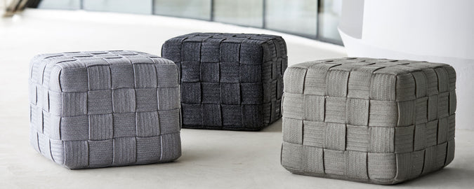 Three stylish cube-shaped poufs in various shades of gray, featuring a woven texture that adds a modern touch to any space.