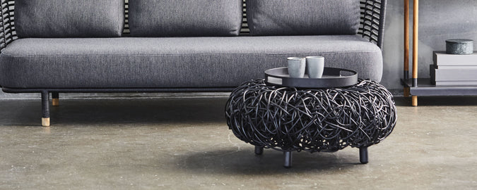 Stylish black loop coffee table with an intertwined design, paired with a gray sofa and two white cups on a sleek surface.