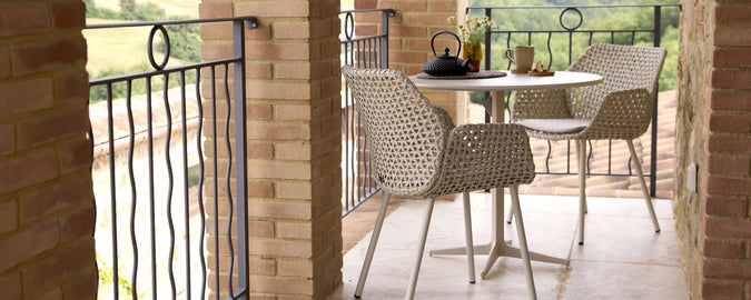 A cozy balcony featuring a round table and two woven chairs, perfect for relaxing with a tea set and enjoying scenic views.