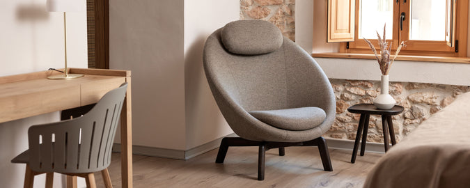 Cozy seating area featuring a modern chair with a rounded design, a small side table, and a minimalist desk. Natural light flows in through a window.