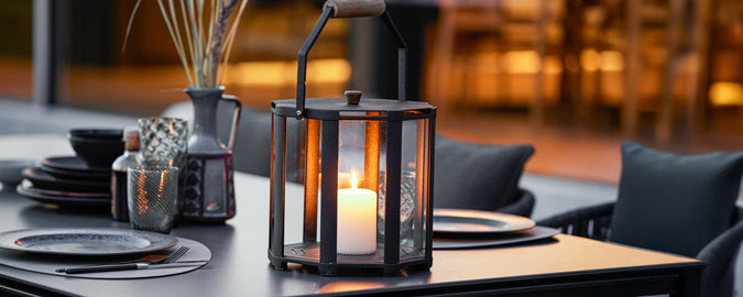Black lantern with candle and black tableware on a modern dining table.