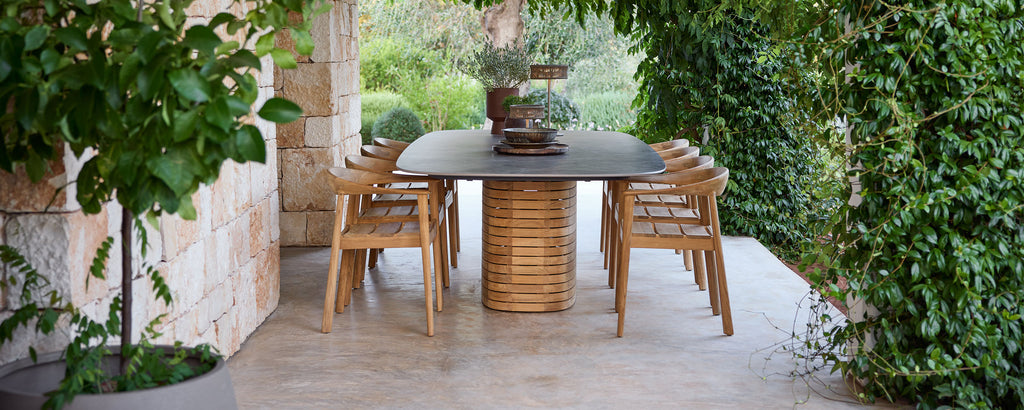 Outdoor wooden dining chairs surrounding a black table in a green garden setting.
