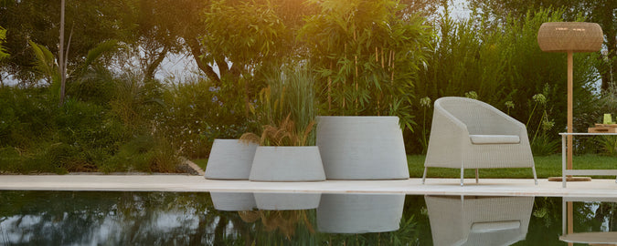 Modern grey chair and planter beside a pool with a brown lamp in an outdoor setting.