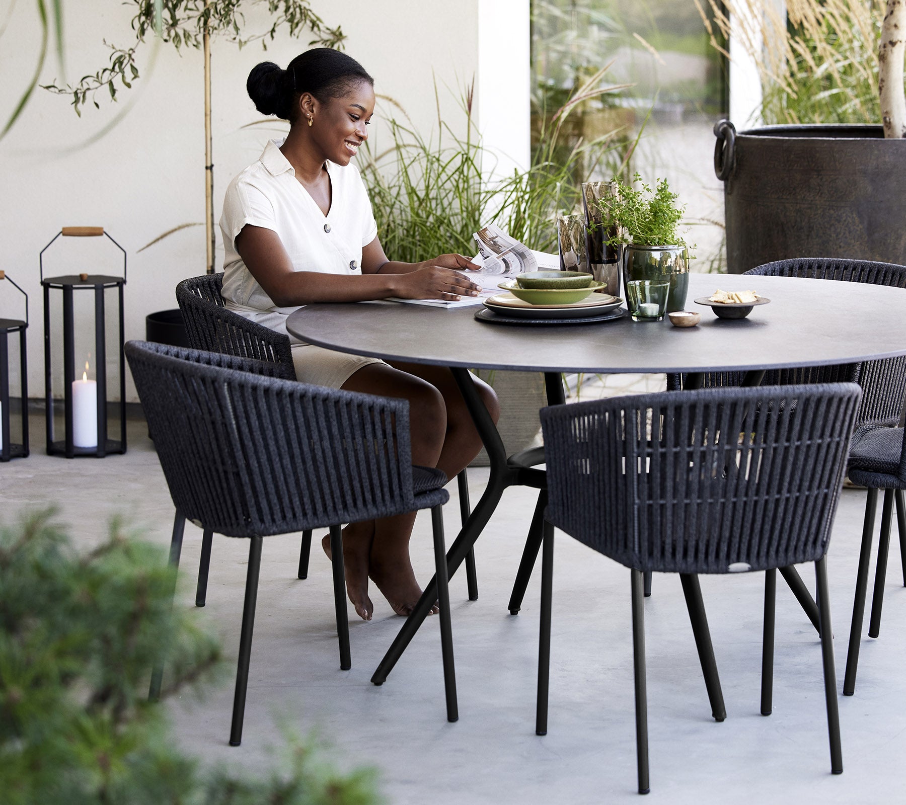 A woman sitting at a round table, enjoying a meal, surrounded by stylish chairs and plants.