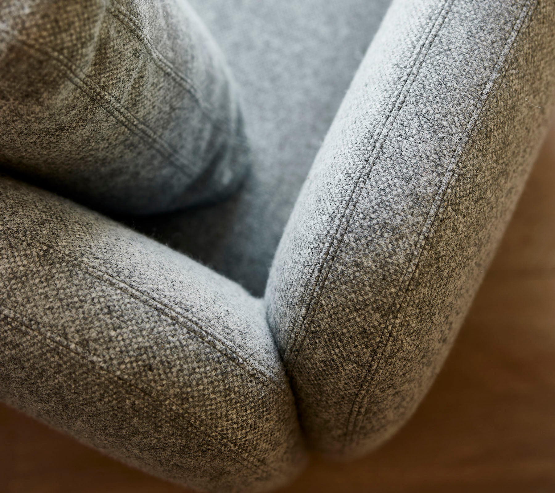 Close-up of a soft, textured gray upholstered armchair, showcasing smooth curves and detailed stitching.
