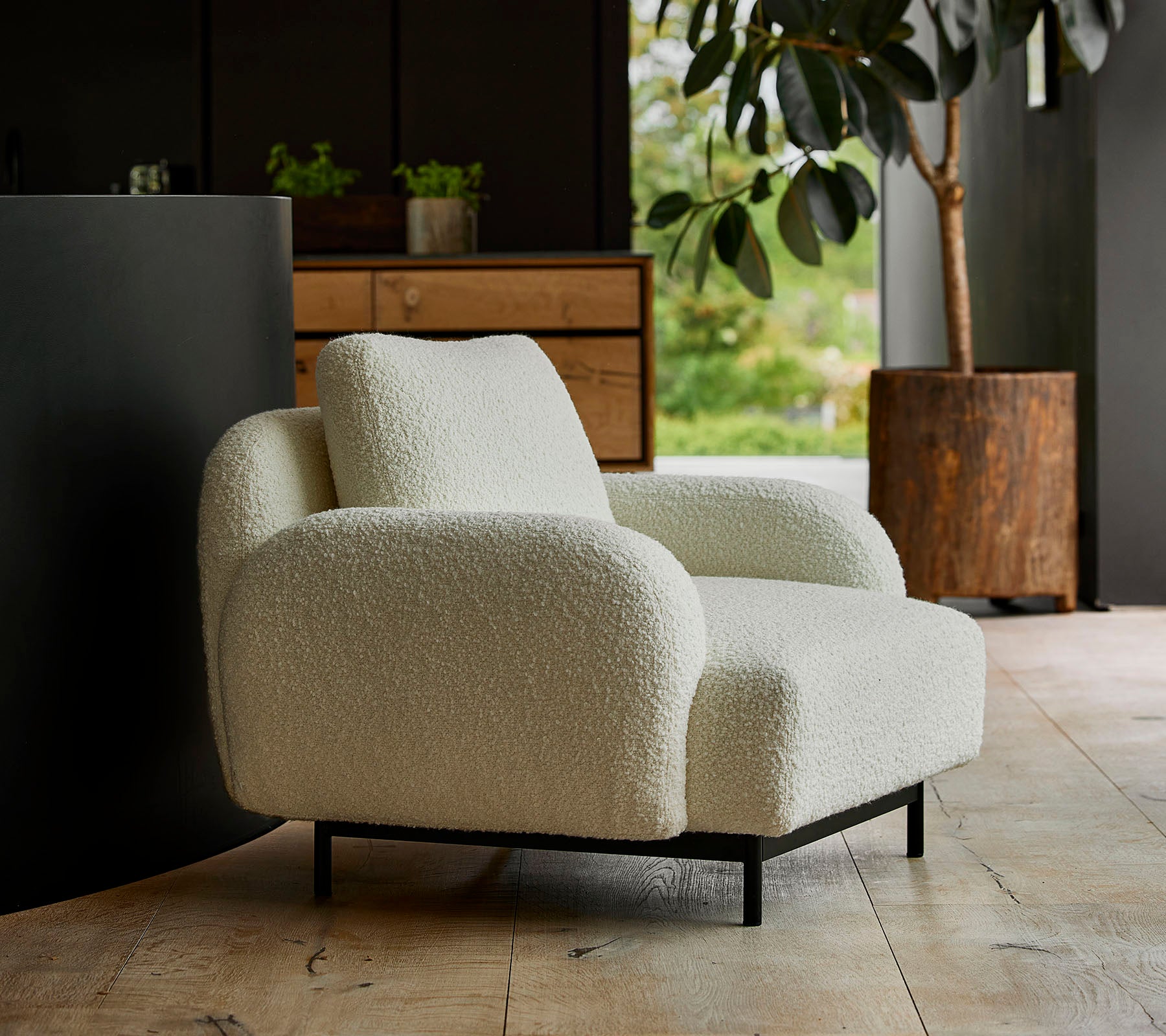 Cozy white lounge chair with rounded armrests and a plush texture, set against a backdrop of greenery and modern furnishings.