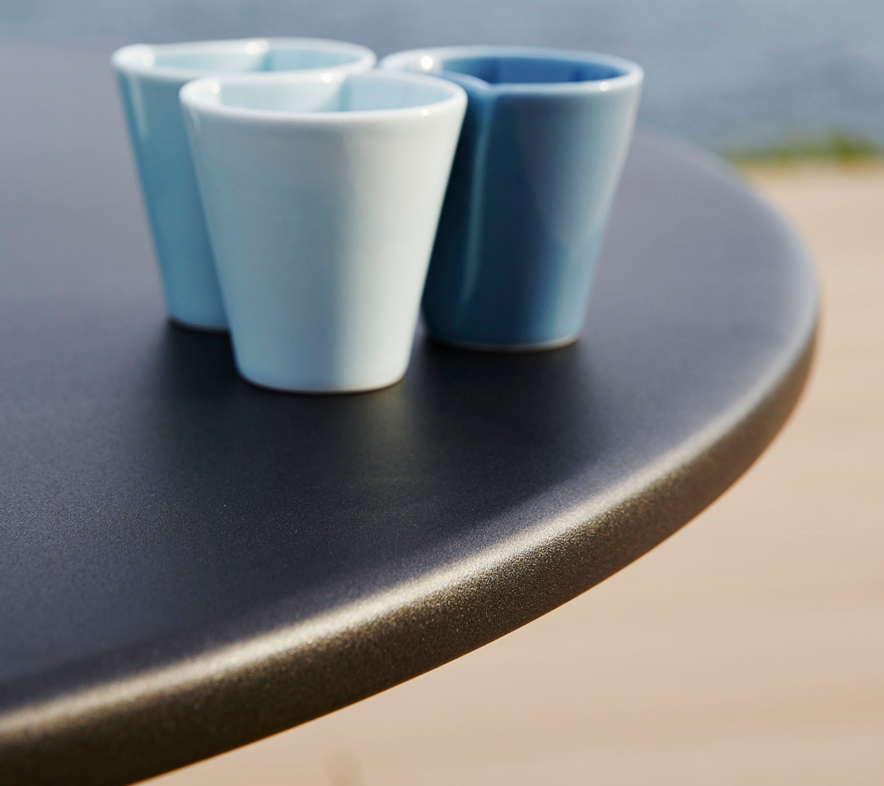 Three small, ceramic cups in varying shades of blue sit on a smooth, round table surface.