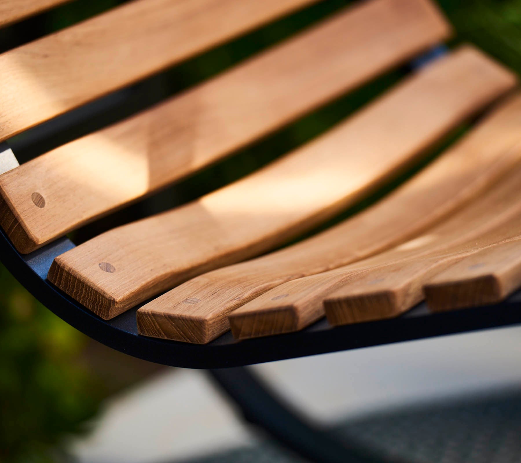 Close-up of a curvy wooden bench slat with smooth, natural wood grain, showcasing craftsmanship and a warm, inviting design.