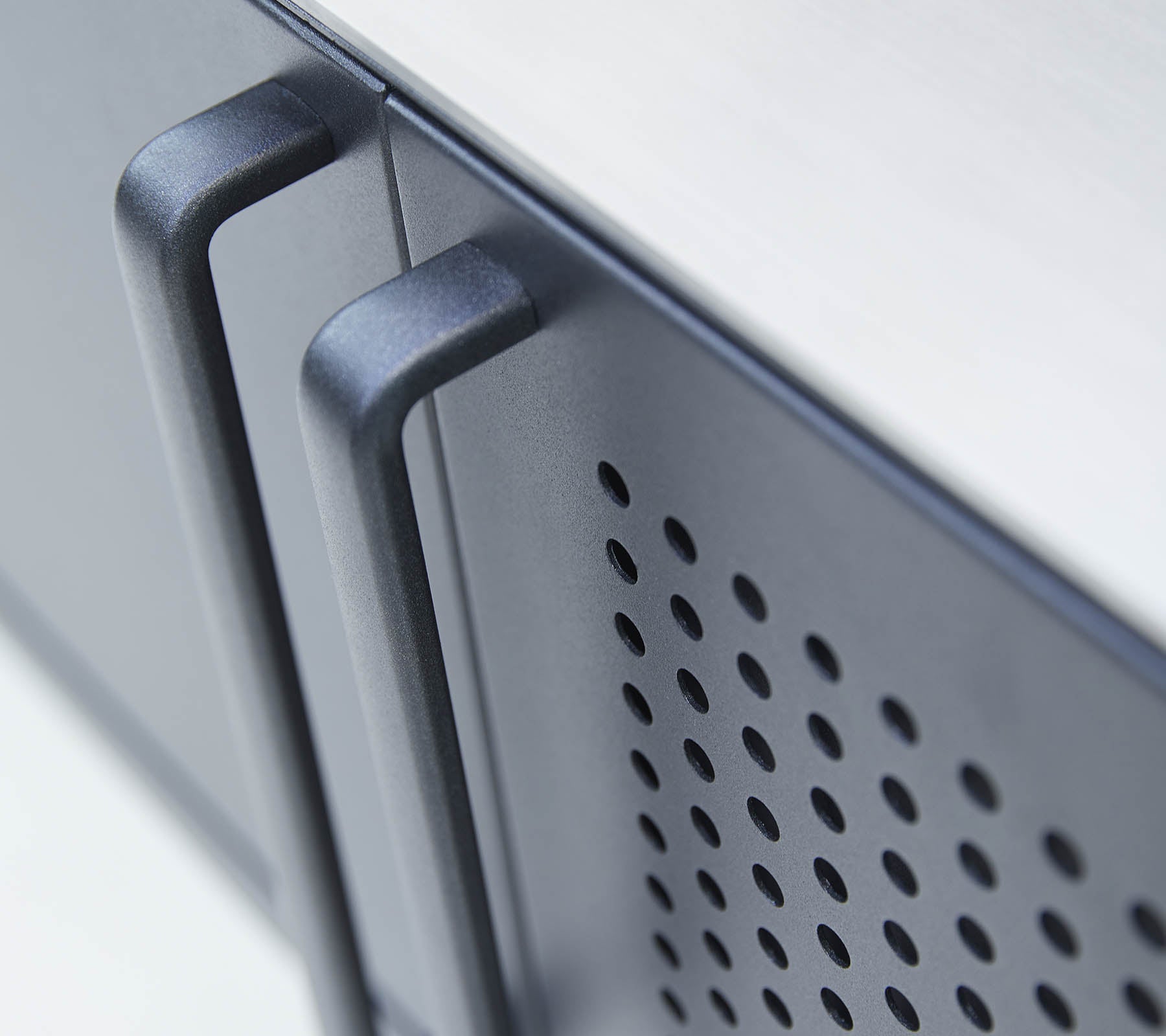 Close-up view of a sleek appliance with two handles and a perforated pattern on the surface, emphasizing modern design features.
