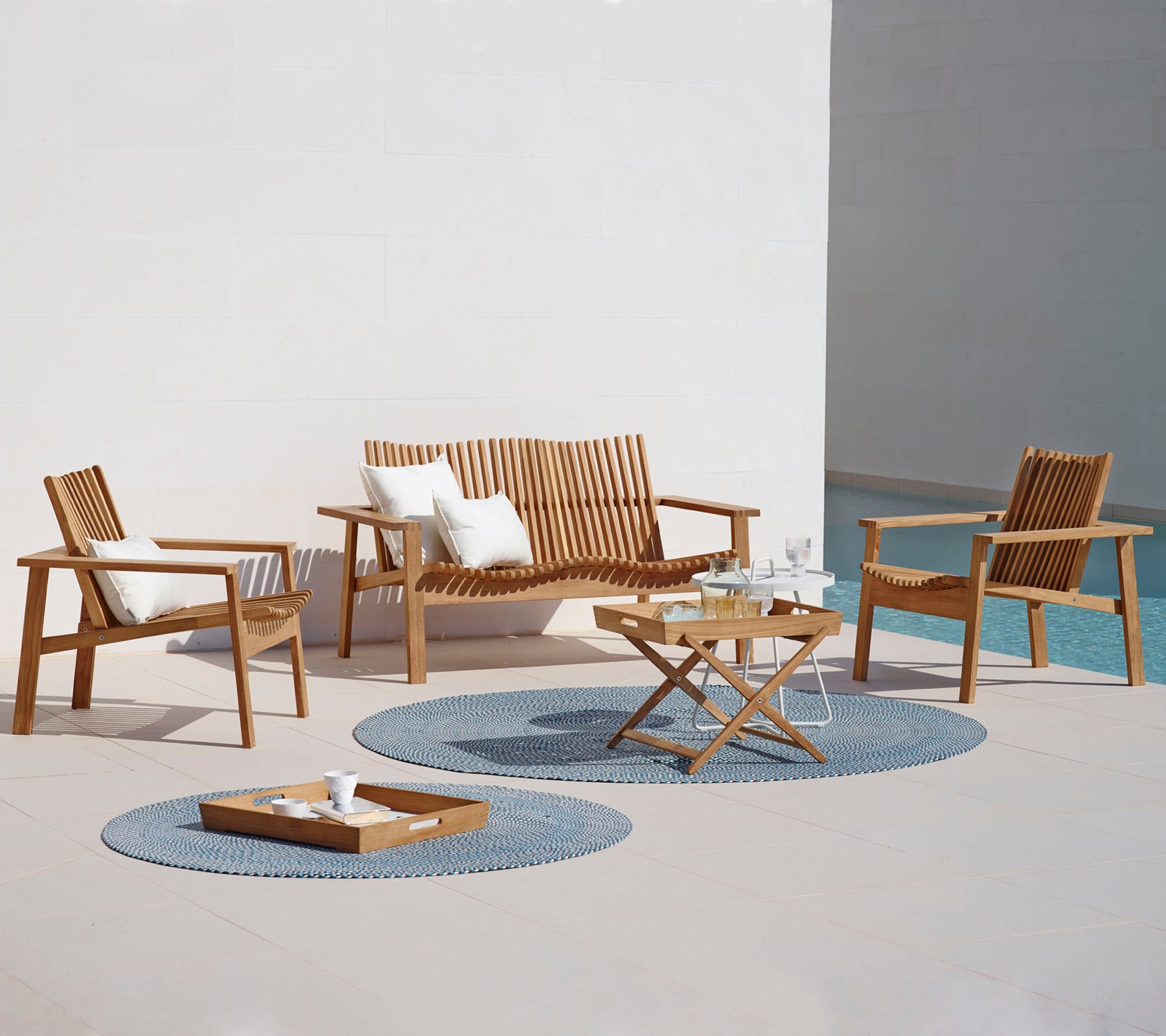 A stylish outdoor seating arrangement featuring a sofa, two armchairs, a coffee table, and decorative rugs. Ideal for relaxation.