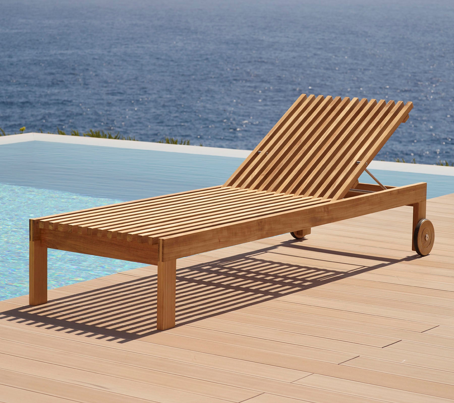 Wooden lounge chair with slatted design, featuring wheels and positioned beside a swimming pool with a water view in the background.