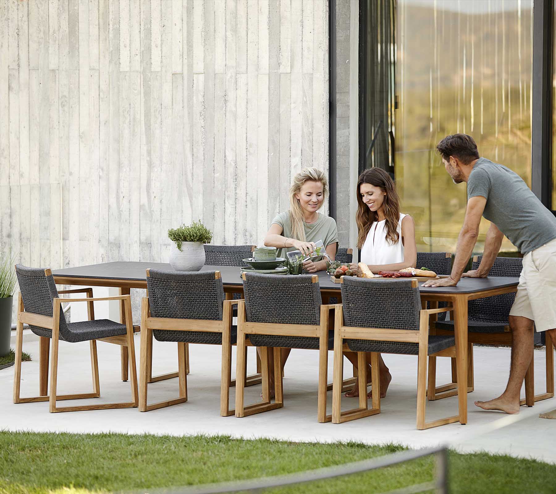 Four people enjoy a meal together at a stylish wooden dining set, featuring modern chairs and a serene outdoor setting.