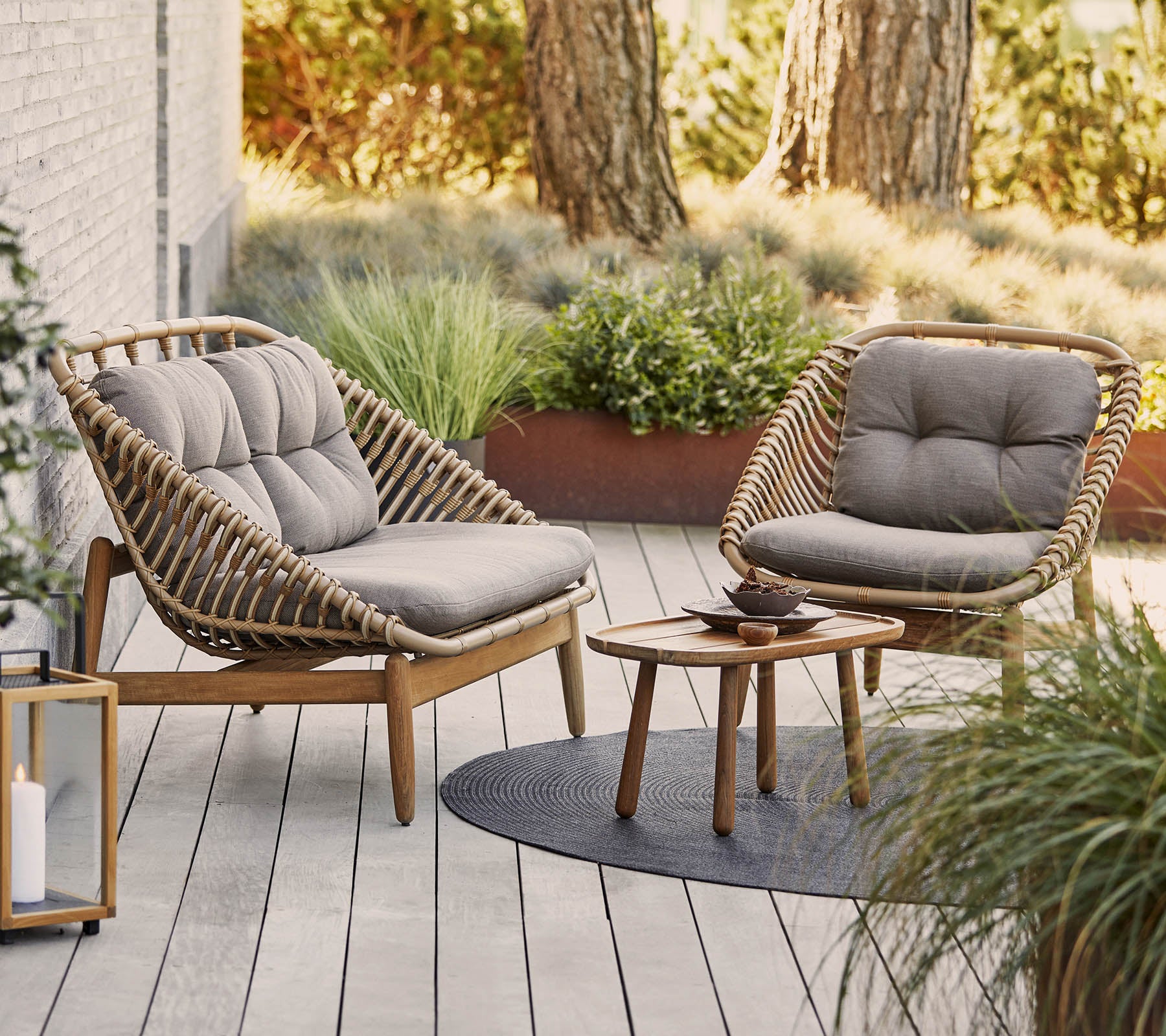 Two stylish chairs with plush cushions surround a small wooden table on a textured surface, complemented by green plants in the background.
