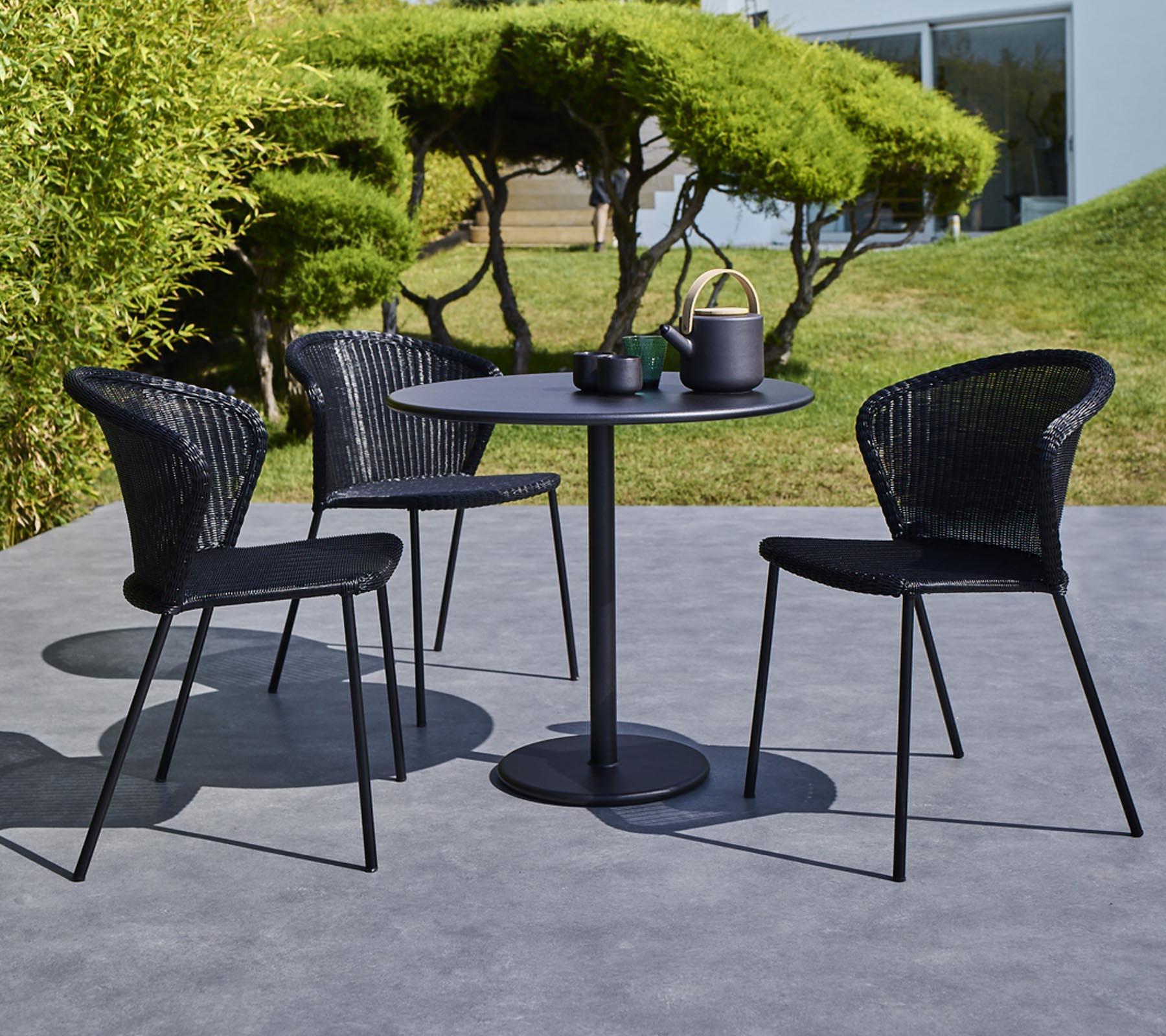 A modern outdoor table set featuring a round table and three black woven chairs, complete with a teapot and cups on the table.