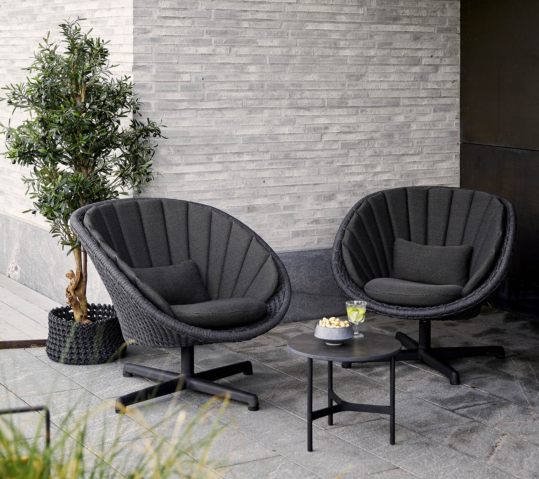 Two stylish, modern chairs with a round design, accompanied by a small table and a potted plant, set against a textured wall.