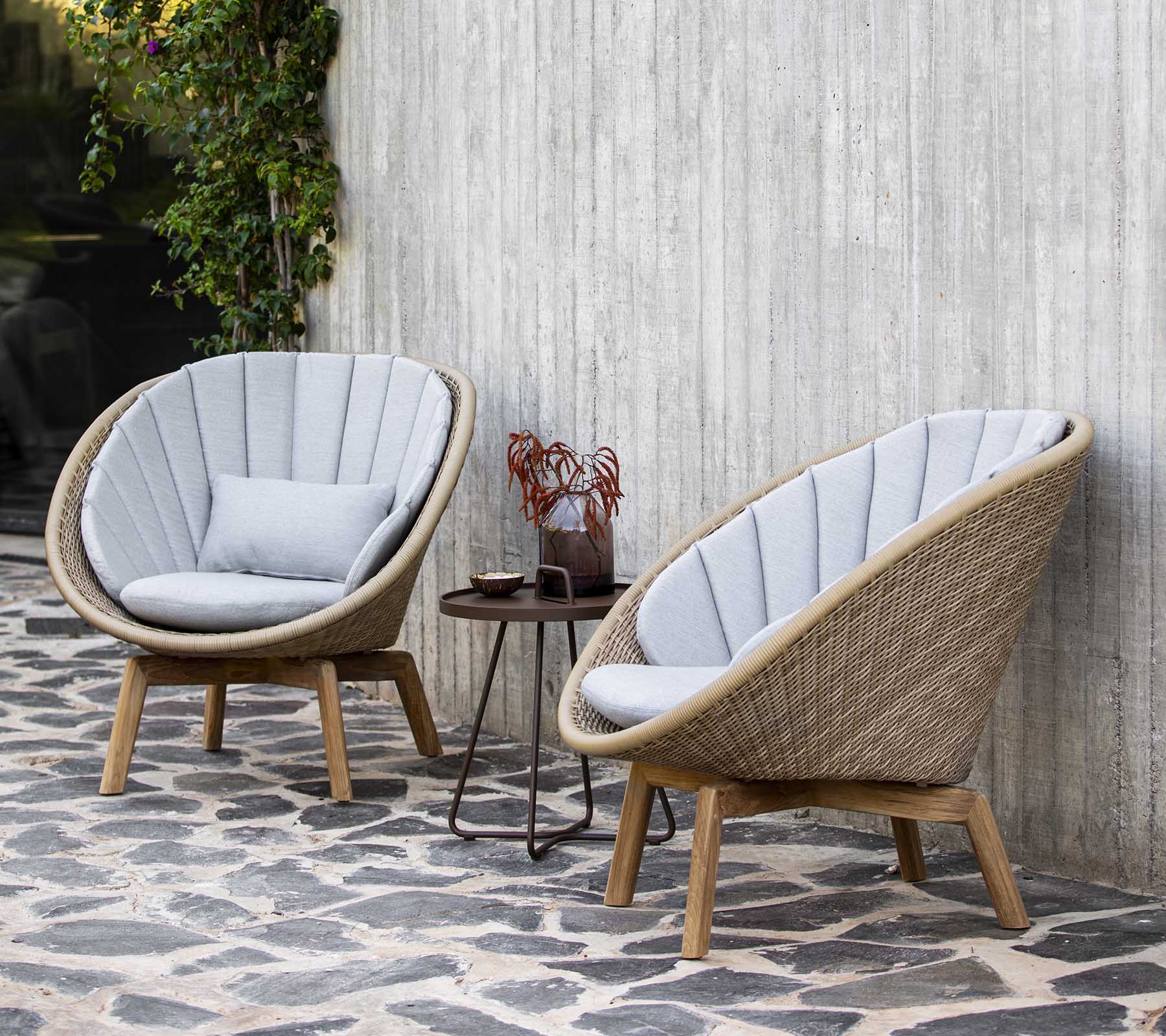 Two stylish, curved armchairs with soft gray cushions beside a small table adorned with decorative items, set against a textured wall.