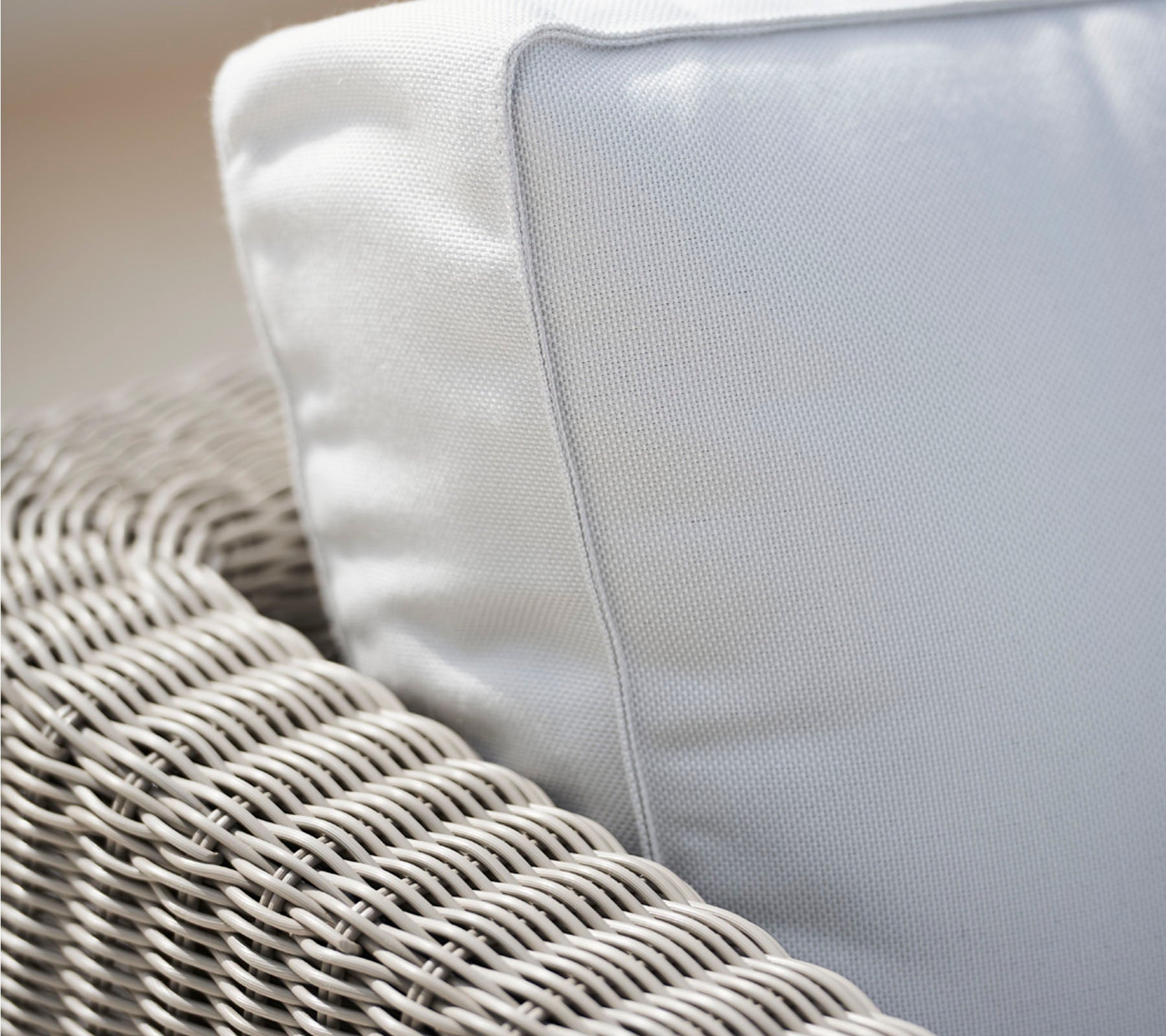 Close-up of a woven chair with a white cushion, highlighting the texture of the wicker and the smooth fabric of the cushion.