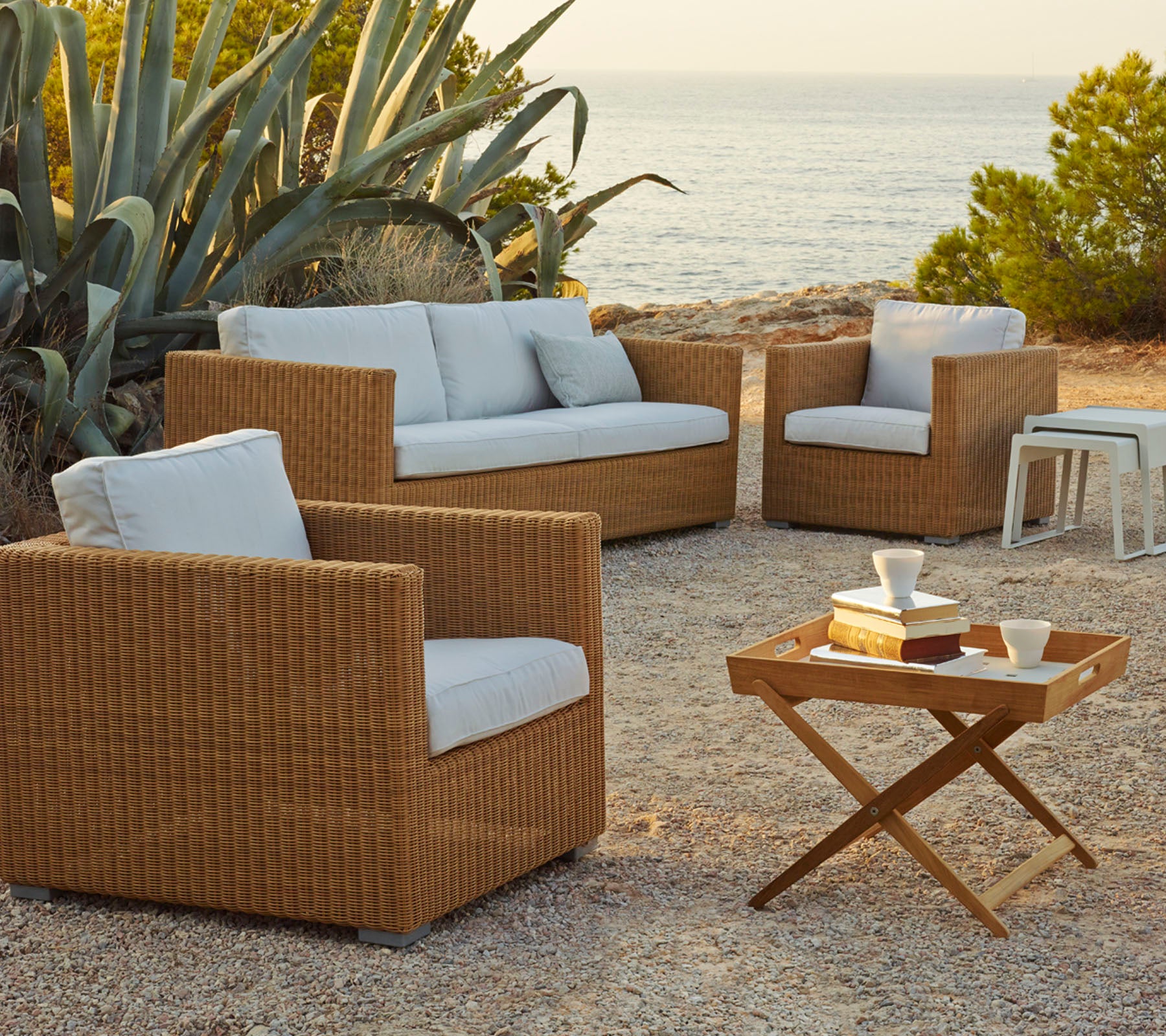 Stylish outdoor seating arrangement featuring woven rattan chairs and a sofa with light cushions, complemented by a wooden coffee table.