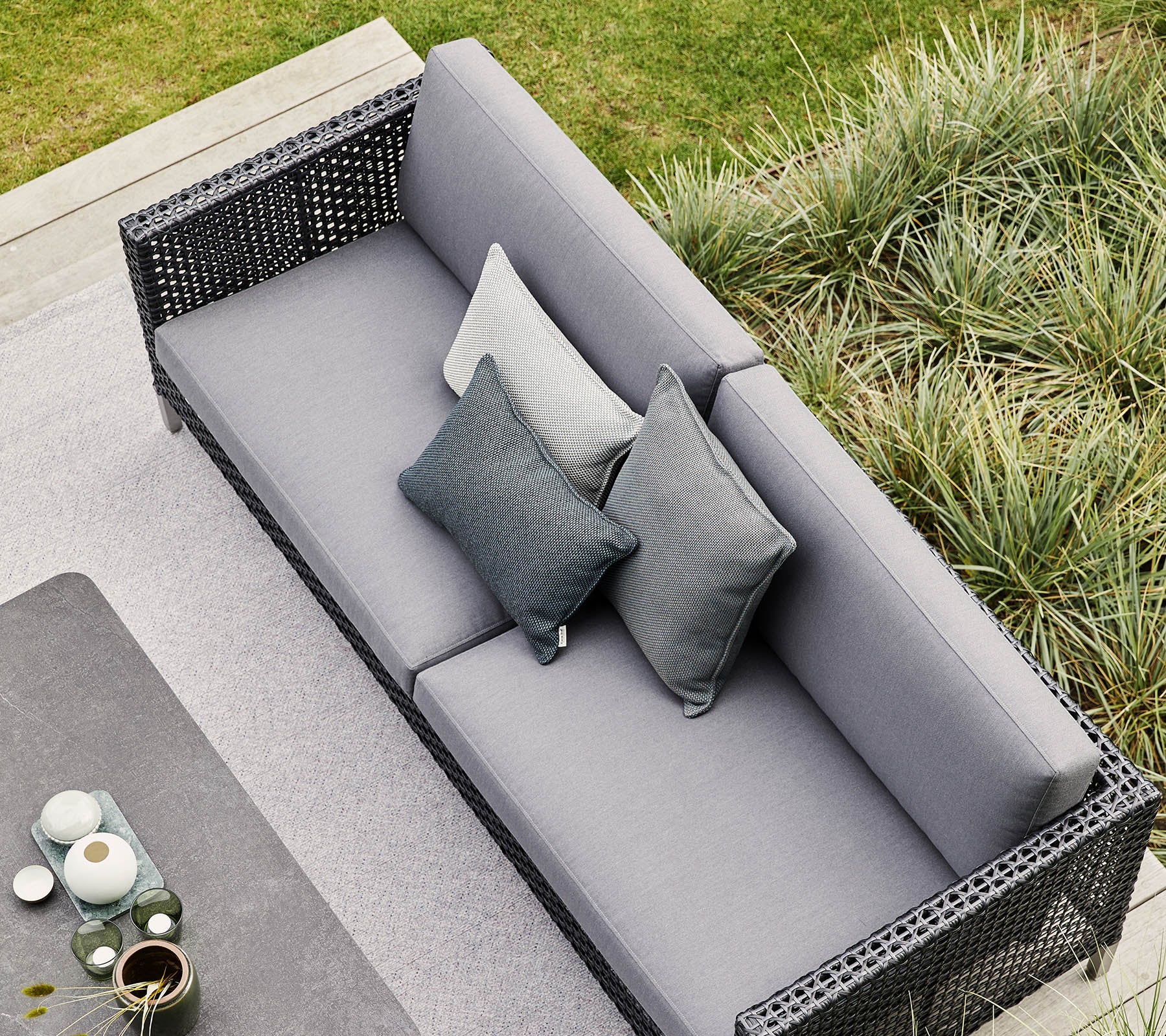 Stylish gray sofa featuring decorative pillows, surrounded by lush greenery and modern decor elements. Perfect for relaxation and gatherings.