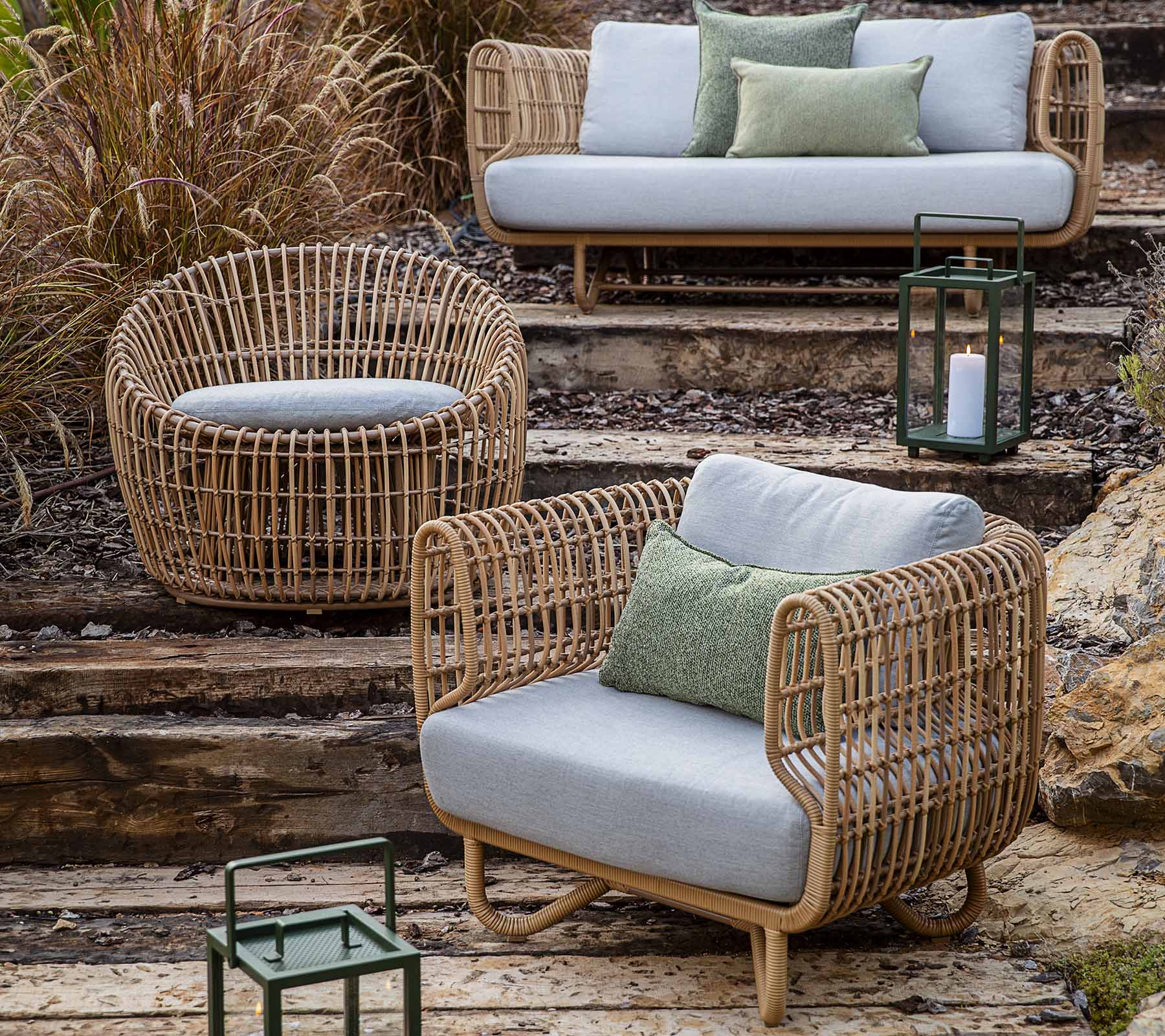 A collection of woven wicker furniture including a sofa, chair, and round seat, accented with cushions and lanterns.