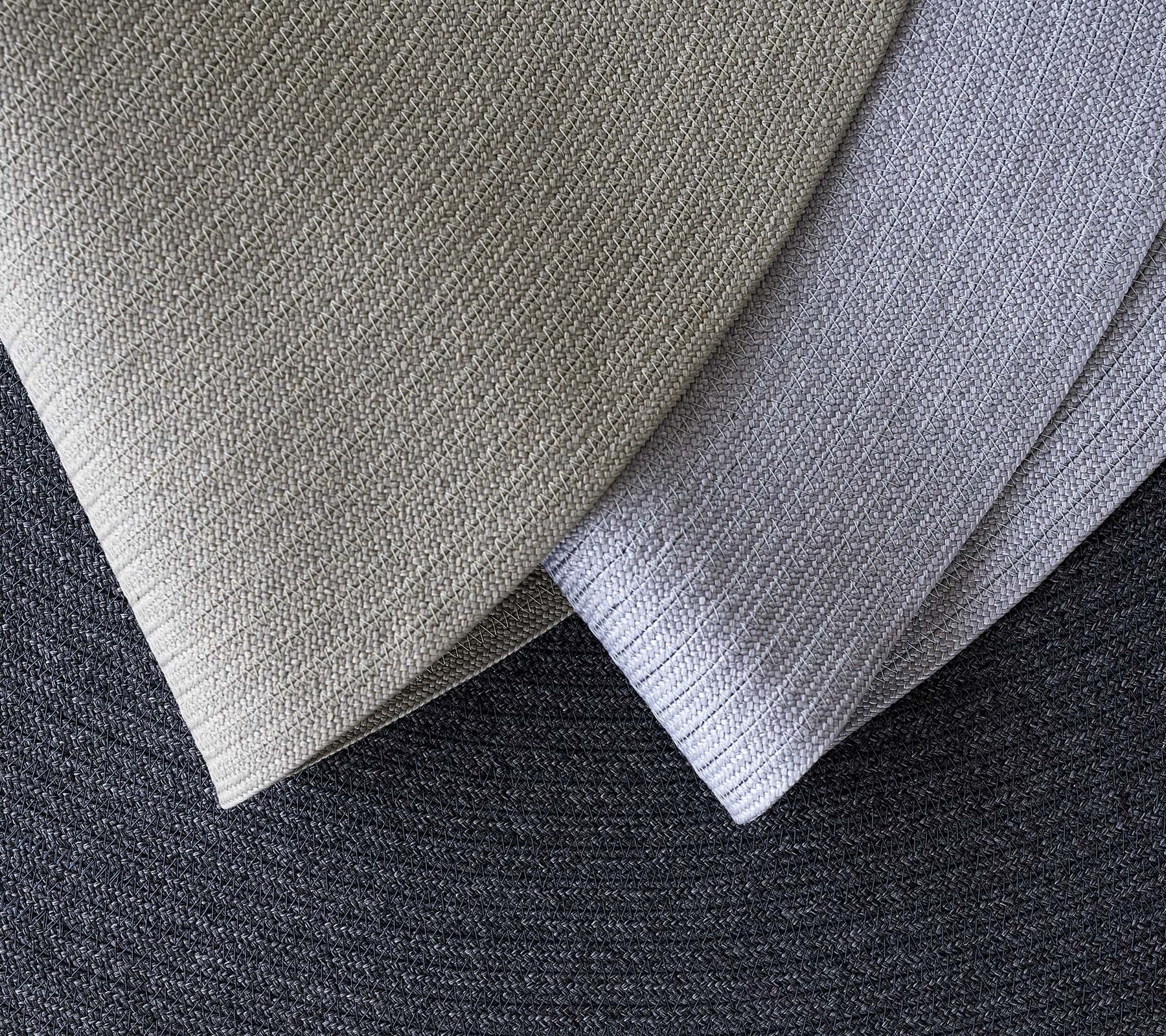 Three overlapping textured fabrics in various shades of gray, showcasing different patterns and tones for design applications.