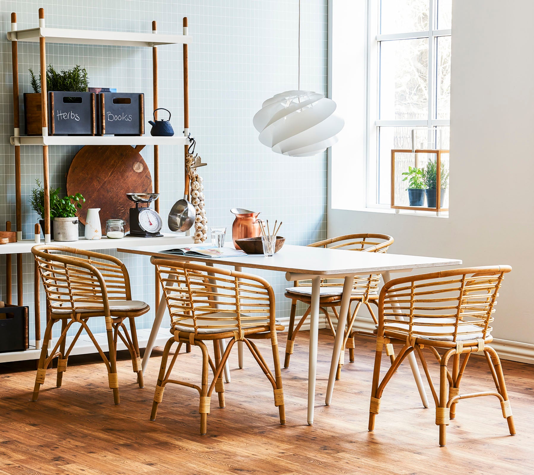 A stylish dining area featuring a light wood table surrounded by rattan chairs and a modern pendant light, complemented by decorative shelving.