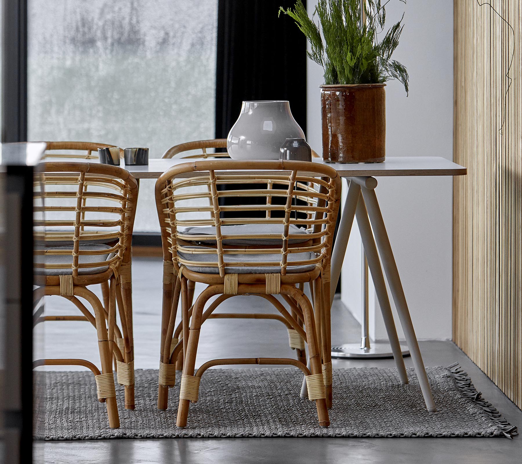 A modern dining setup featuring rattan chairs, a sleek table, and decorative greenery in a stylish interior.