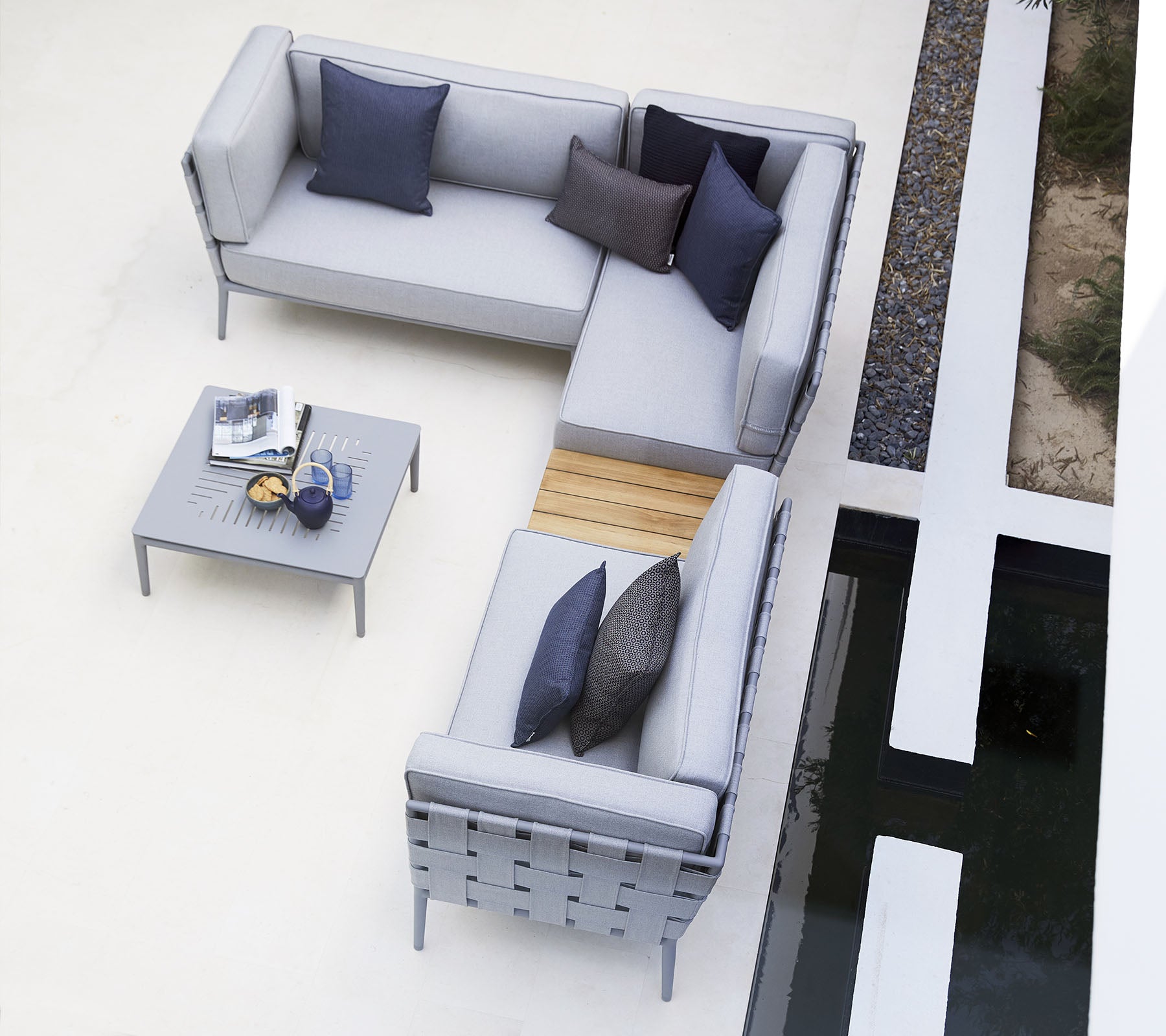 Modern outdoor seating arrangement with gray cushions, accented by dark pillows, complemented by a minimalist table.