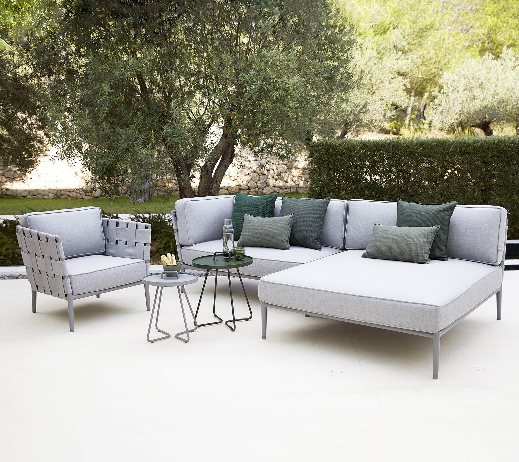 Modern outdoor seating arrangement featuring a sectional sofa with cushions, a chair, and a small glass-top table surrounded by greenery.
