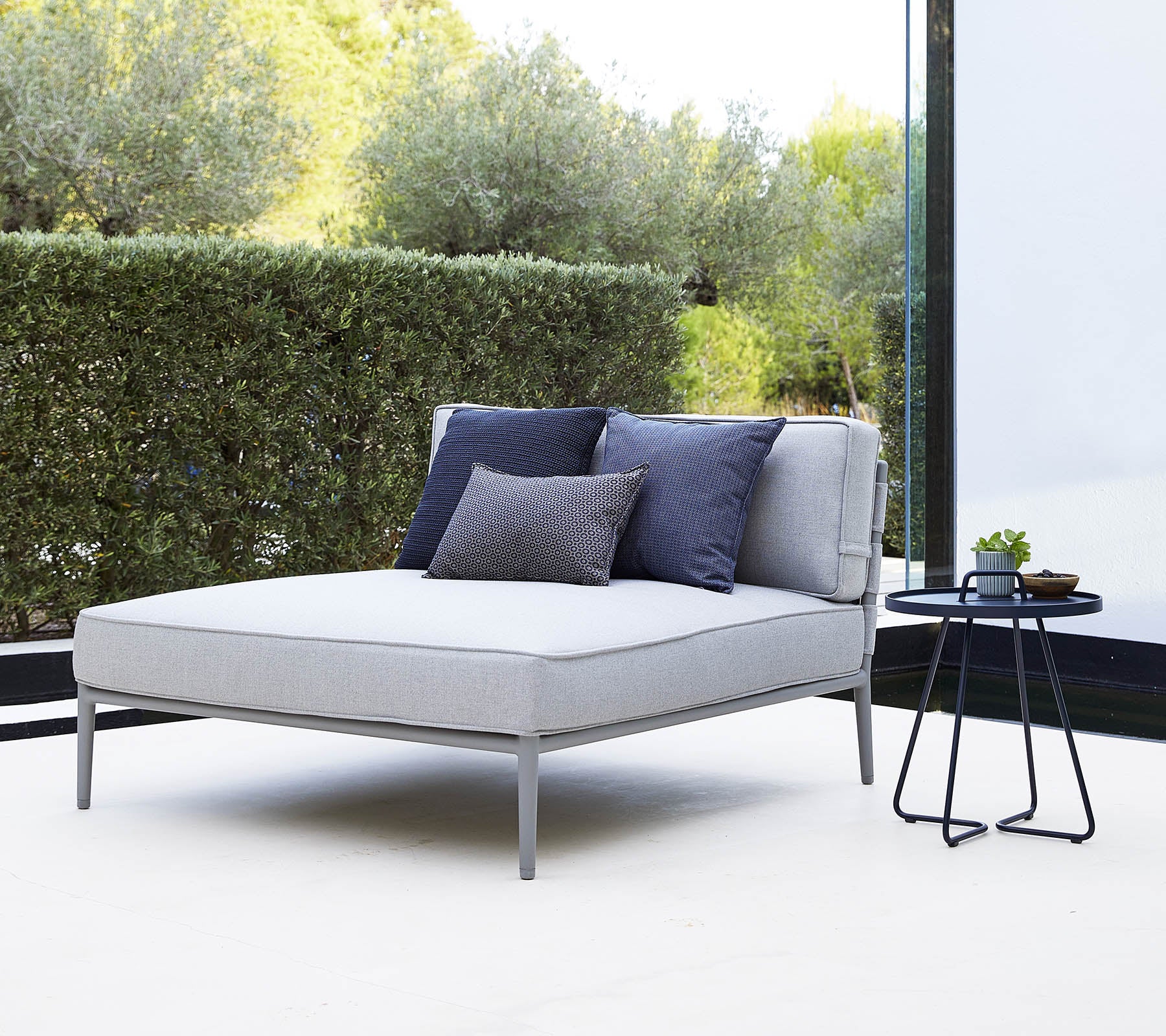 Stylish gray lounge chair with navy cushions beside a small black side table in a serene setting.