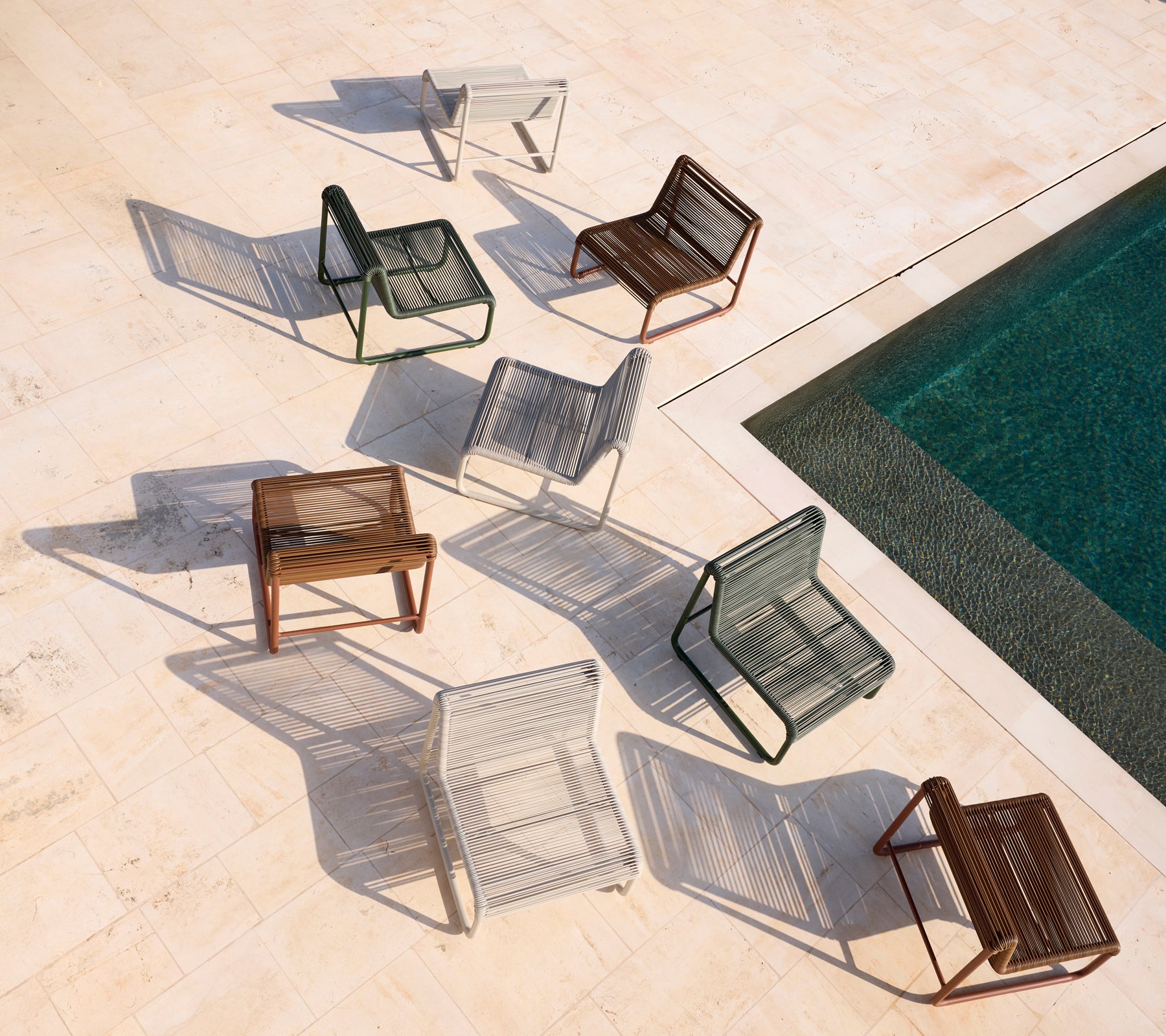 Assorted modern chairs in brown, grey, white, and black arranged around a pool.
