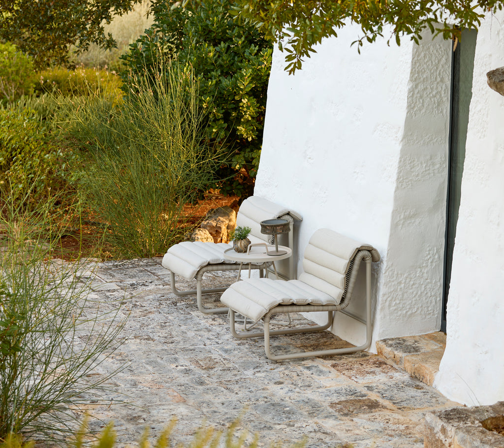 Outdoor modern lounge chairs with grey cushions and a small side table.