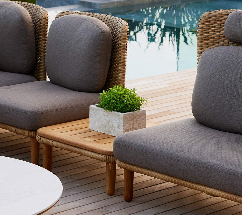 A stylish Arch coffee table with a teak table top, flanked by lounge chairs and a small potted plant, enhancing a chic outdoor setting.