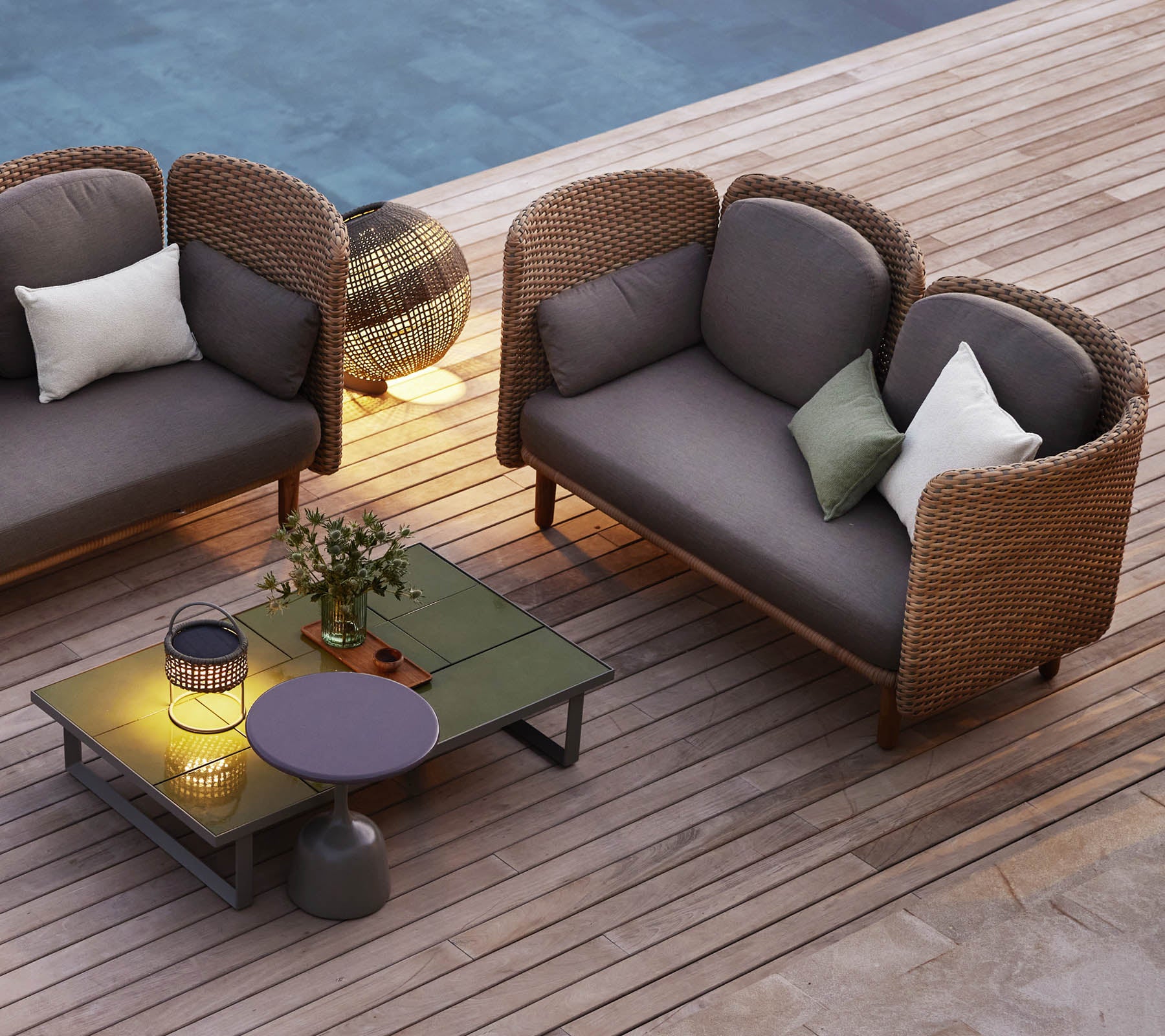 A cozy seating area featuring two curved lounge sofas, a low table, decorative cushions, and ambient lighting.