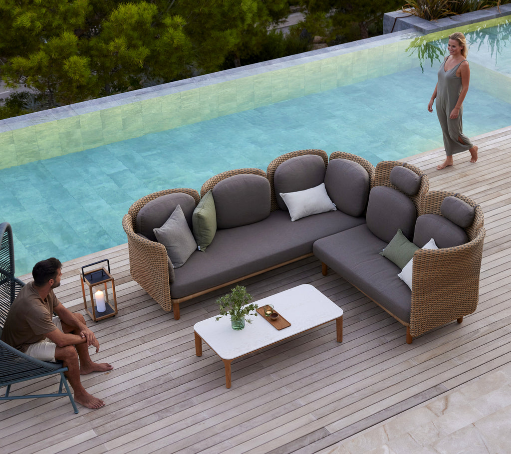 A modern arch sofa with plush cushions and a white coffee table, surrounded by greenery and a serene water feature.