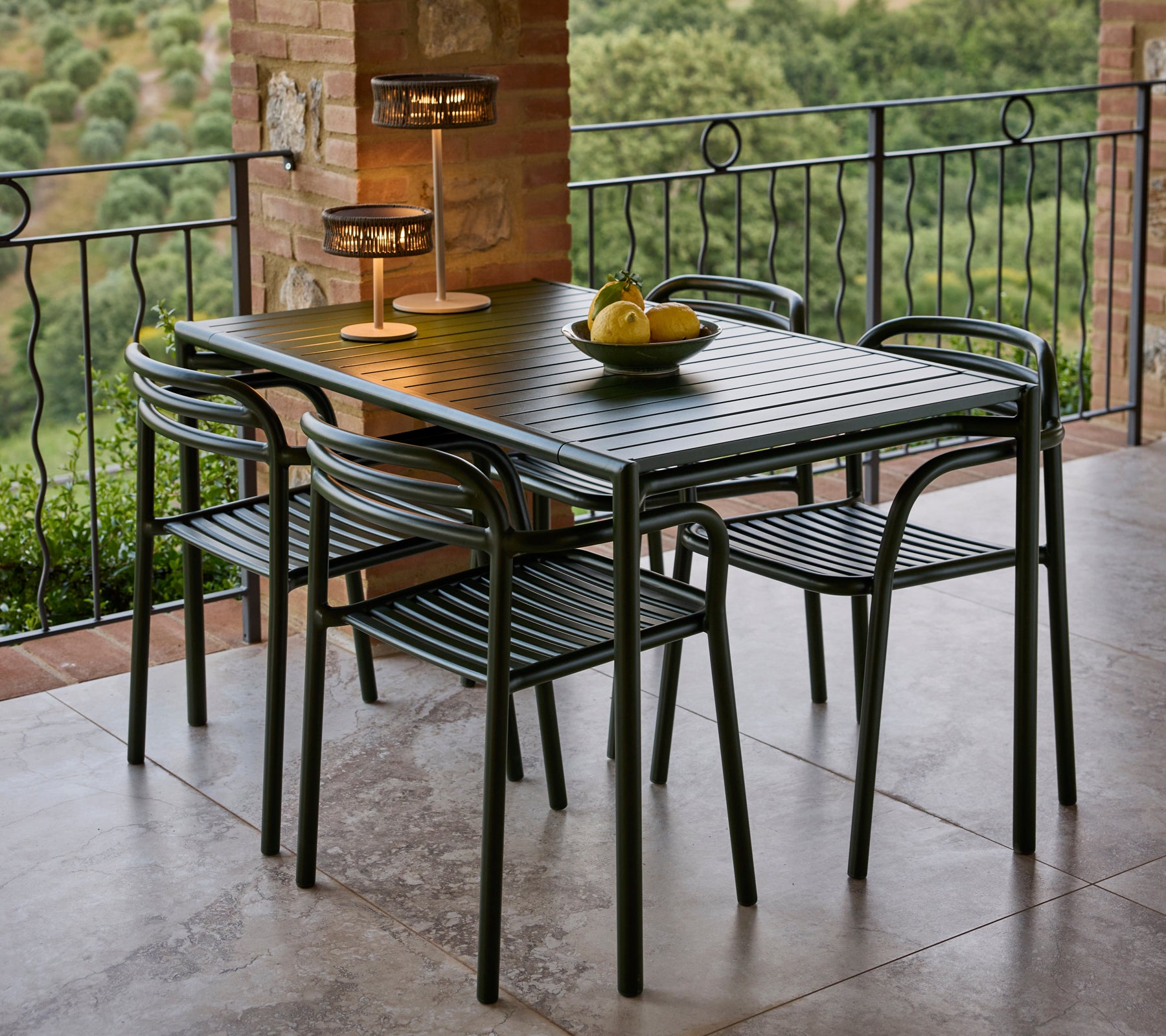 A stylish dining set featuring a sleek table, four chairs, and an elegant lamp, complemented by a decorative fruit bowl.