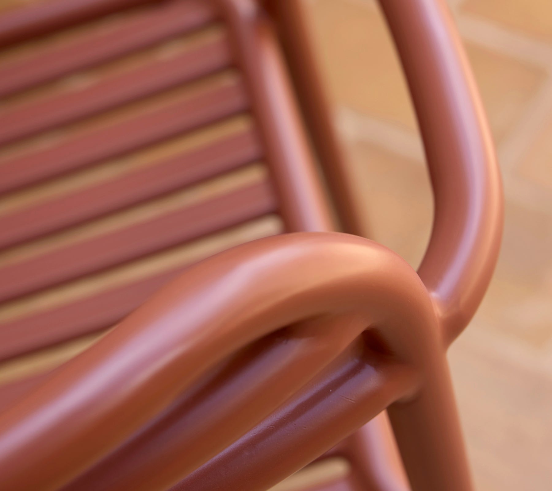 Close-up of a Bliss armchair in a desert red hue, showcasing its smooth curves and slatted design.