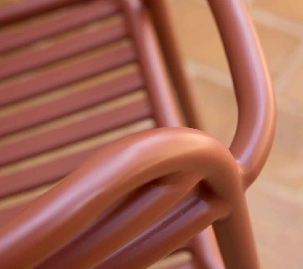 Close-up of a Bliss armchair in a desert red hue, showcasing its smooth curves and slatted design.