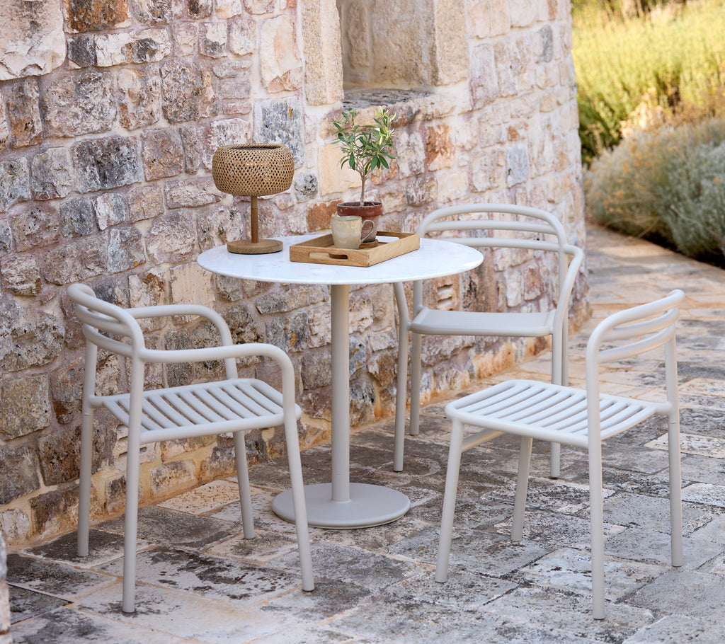 Modern white table with two matching chairs in a rustic outdoor setting.