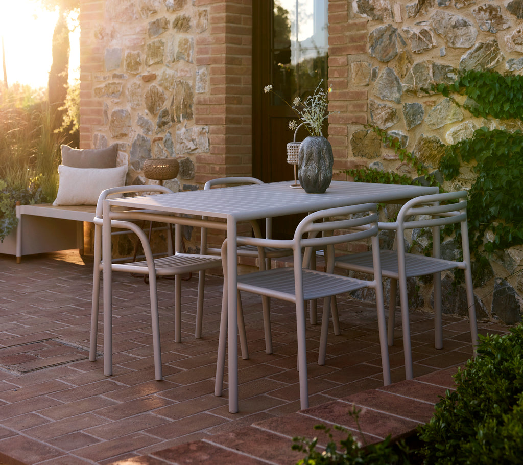 A stylish table set with four chairs, featuring a modern design in a soft sandy color, complemented by a decorative vase.