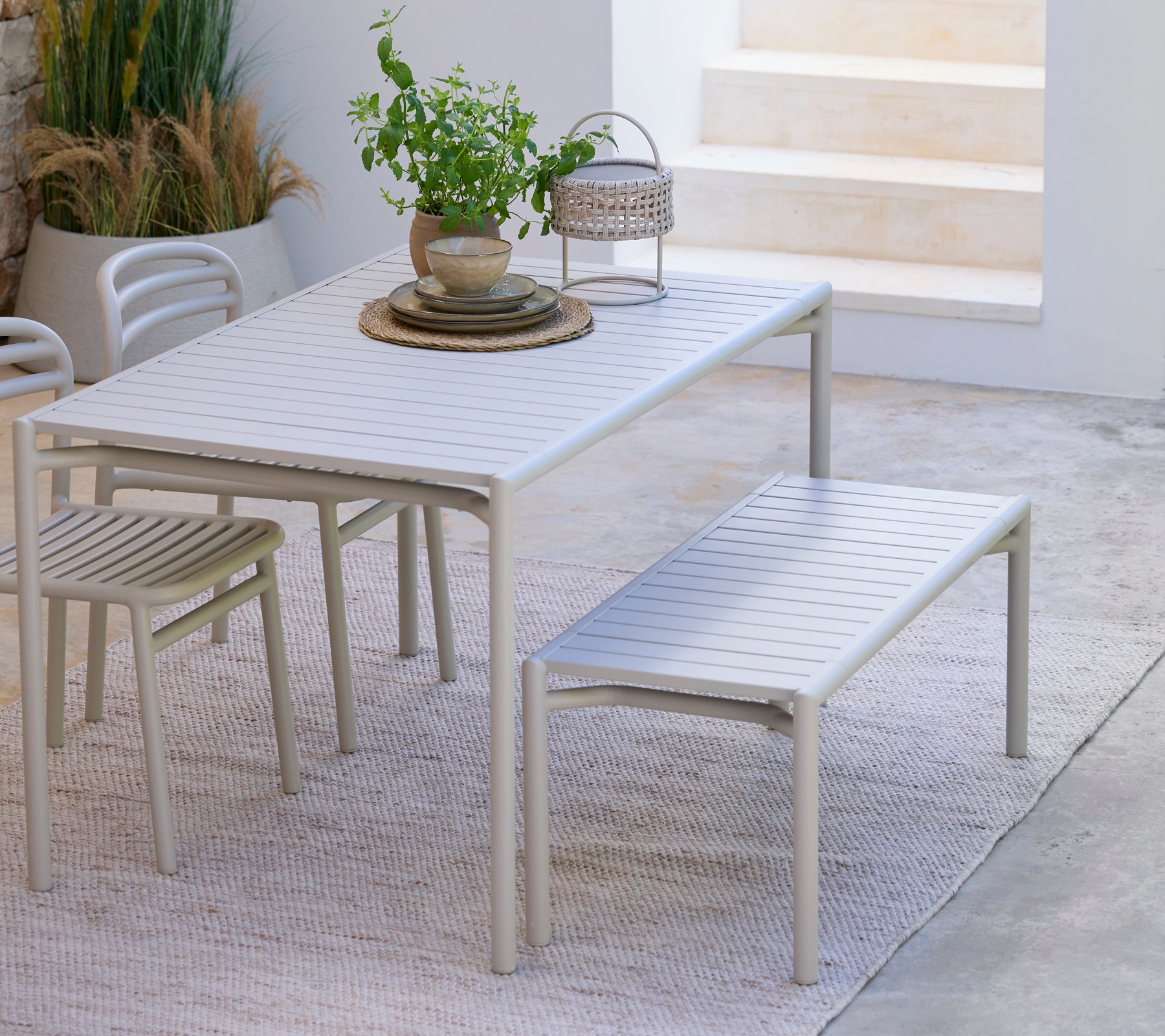 Modern white dining table with matching bench and chair in a minimalist setting.