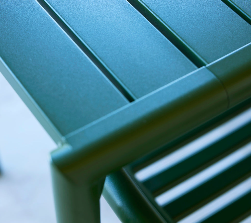Close-up of a green table corner with sleek, horizontal slats and a polished finish, showcasing modern design and functionality.
