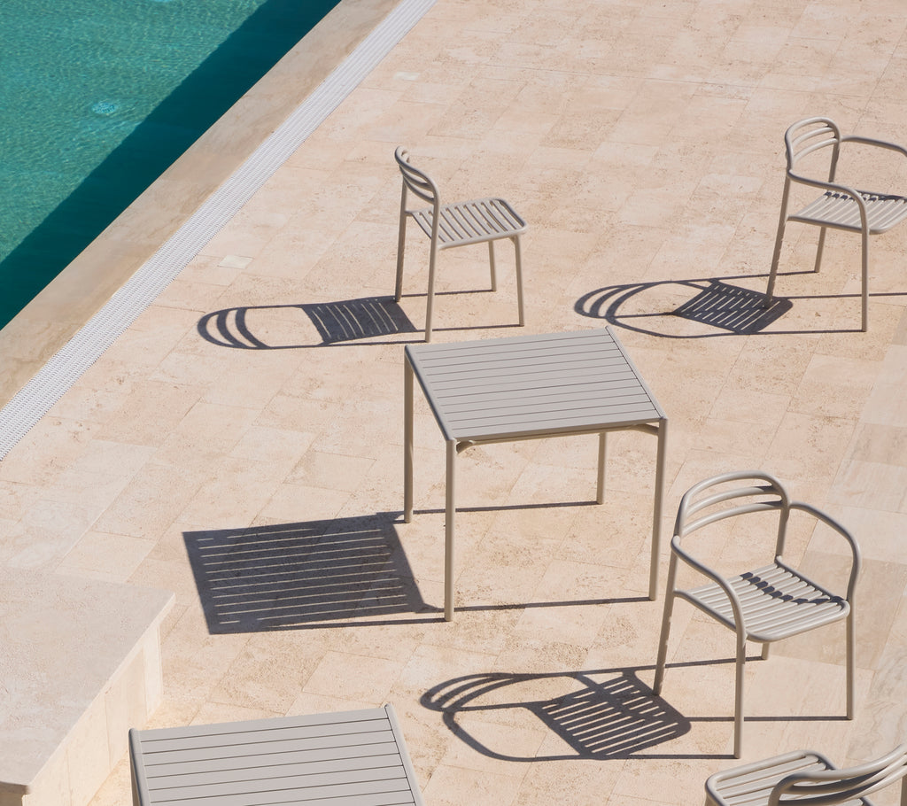 A minimalist table surrounded by elegant dining chairs casting shadows on a warm-toned surface. 