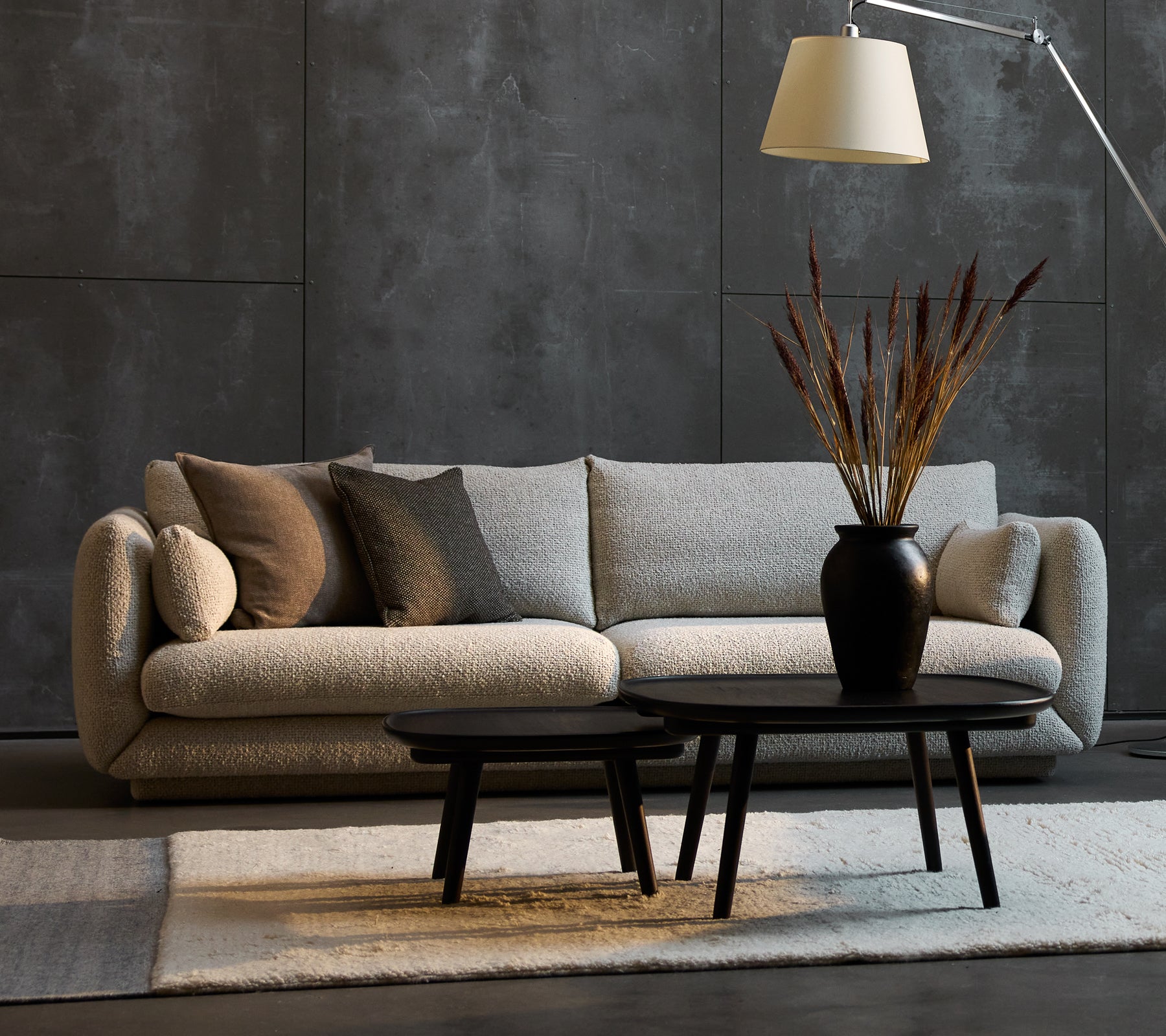 Bloom 3-seater sofa in sand flair with decorative pillows, accompanied by two Pace coffee tables of varying sizes and a stylish floor lamp.