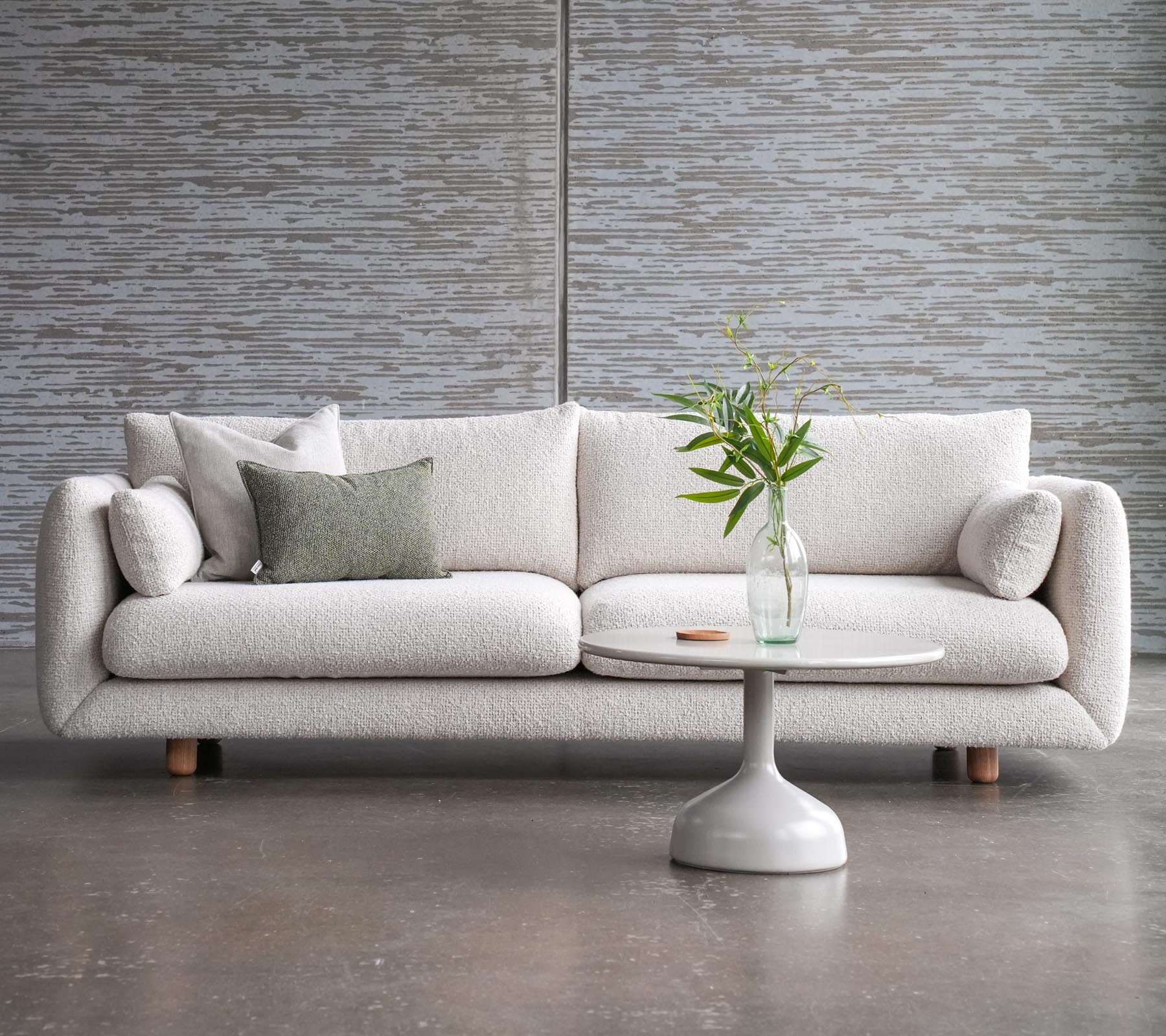 A stylish sofa with cushions beside a Glaxe coffee table featuring a round top and elegant teak legs, adorned with a vase of flowers.