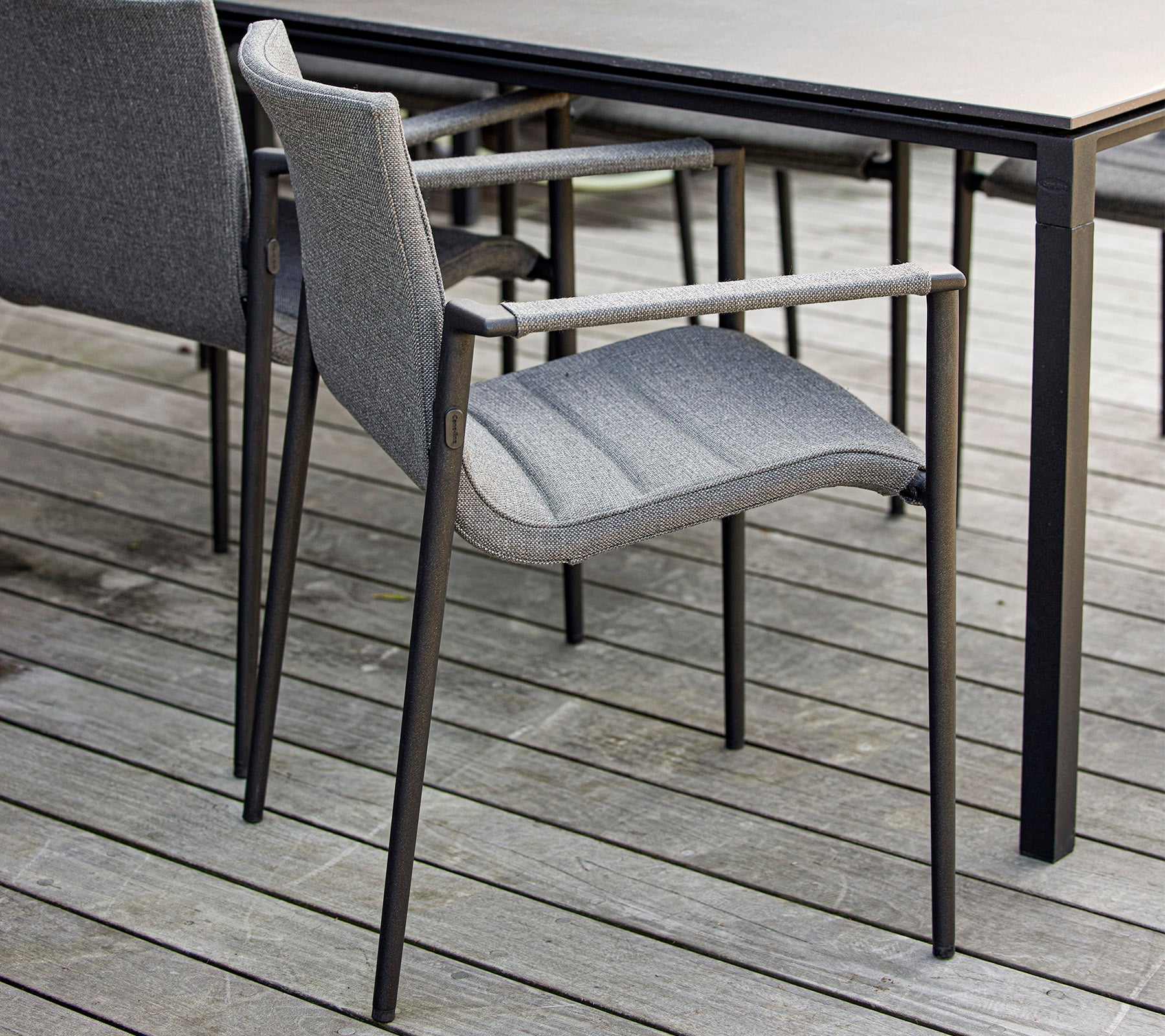 Stylish gray chair with armrests positioned next to a sleek black table on a wooden surface. Ideal for modern outdoor settings.