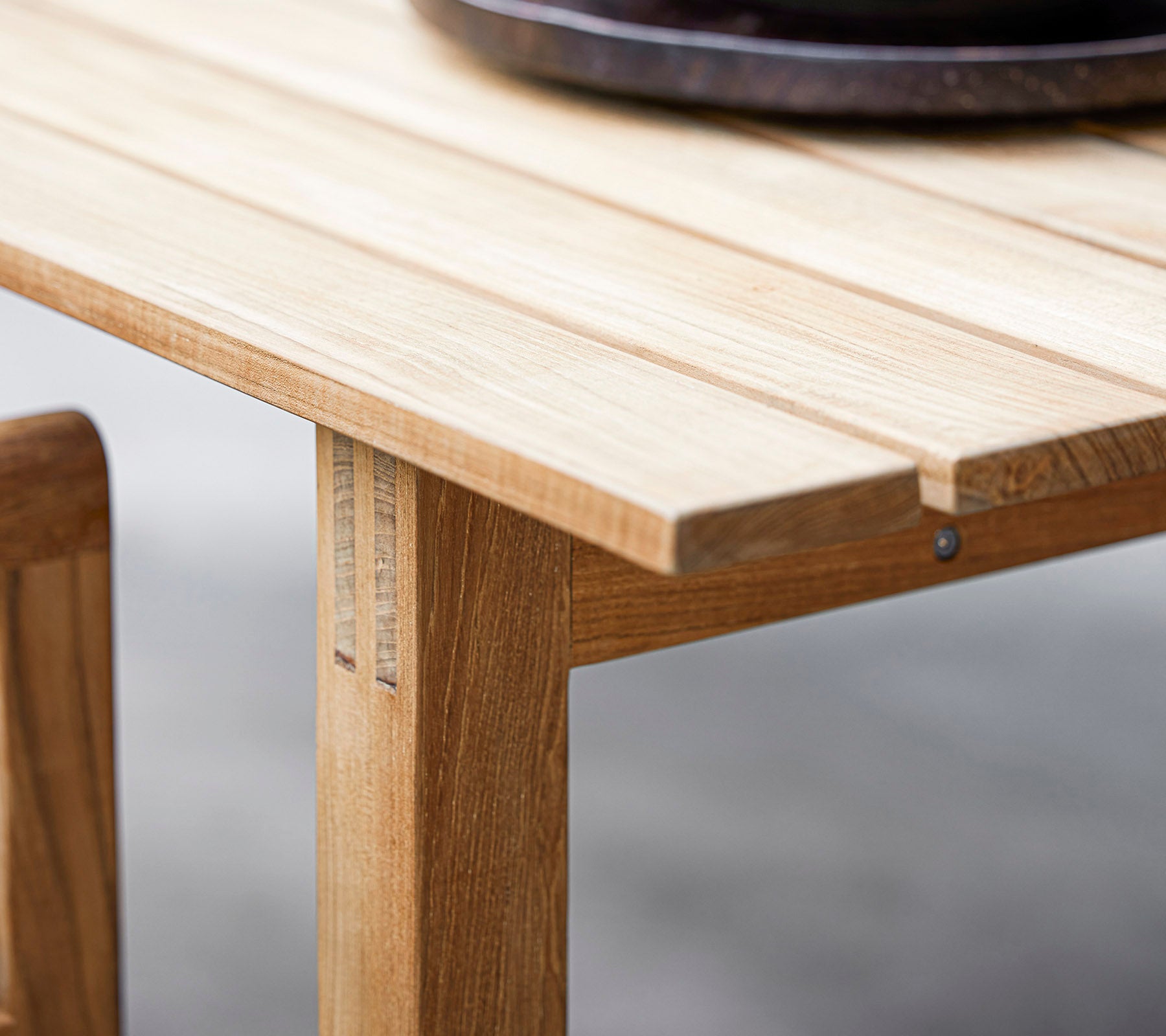 Close-up of a wooden table showcasing slatted design and a dark round decorative bowl on top. Perfect for modern dining aesthetics.