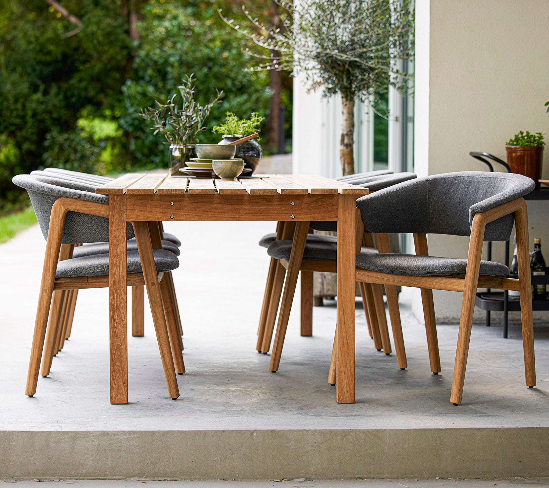 A stylish wooden dining table surrounded by four grey cushioned chairs, perfect for outdoor gatherings.